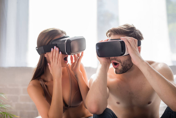 σοκαριστικό ζευγάρι που χρησιμοποιεί και αγγίζει ακουστικά VR στην κρεβατοκάμαρα - Φωτογραφία, εικόνα