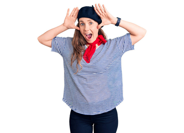 Young beautiful blonde woman wearing french beret and striped t-shirt smiling cheerful playing peek a boo with hands showing face. surprised and exited  - Photo, Image