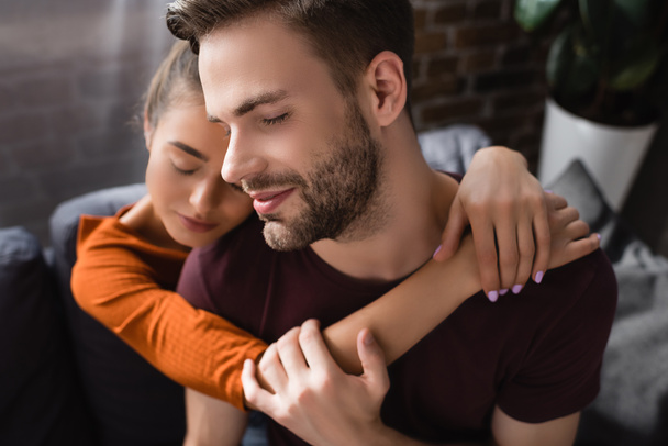 young man with closed eyes embraced by tender girlfriend on blurred background - Photo, Image
