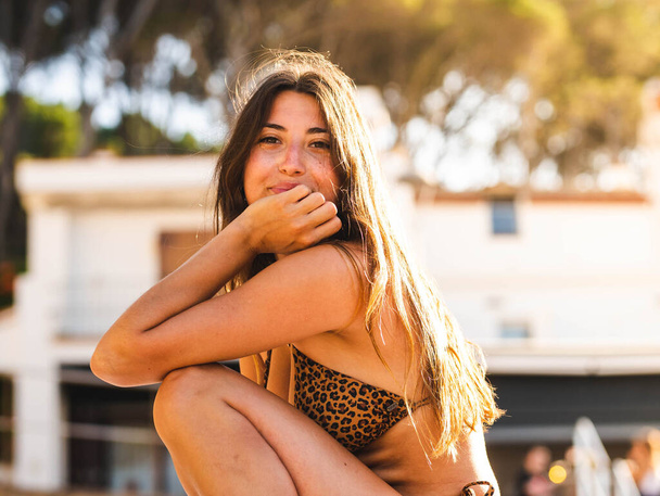 attraktive Kaukasierin im Bikini, die lächelt. Kaukasische Hündin mit Leopardenmuster sitzt am Strand - Foto, Bild