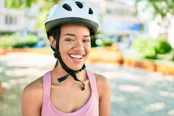 Junge schöne hispanische Radfahrerin lächelt glücklich mit Fahrradhelm in der Stadt - Foto, Bild