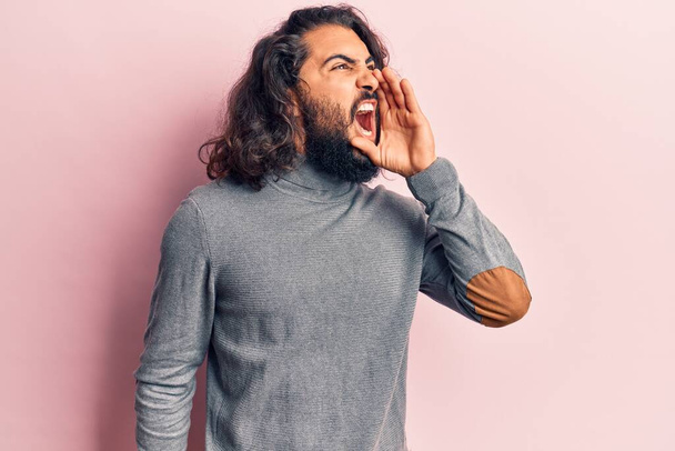 Jonge Arabier man draagt nonchalante kleren schreeuwend en schreeuwend met hand op mond. communicatieconcept.  - Foto, afbeelding