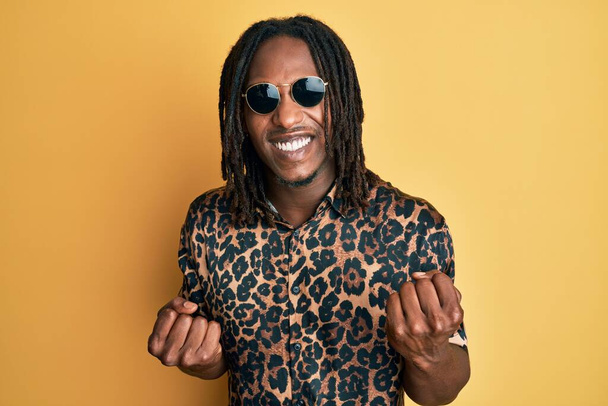 Αφροαμερικανός άνδρας με κοτσίδες φορώντας animal print πουκάμισο και γυαλιά ηλίου γιορτάζει έκπληκτος και έκπληκτος για την επιτυχία με τα χέρια ψηλά και τα μάτια κλειστά  - Φωτογραφία, εικόνα