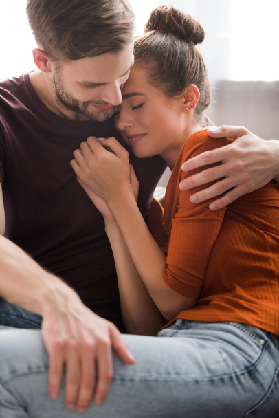 young man embracing upset girlfriend while calming her at home - Fotó, kép