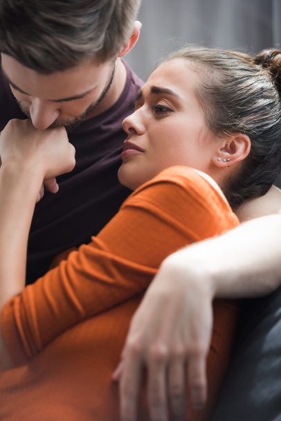 responsive man kissing hand of upset girlfriend while calming her at home - Photo, Image