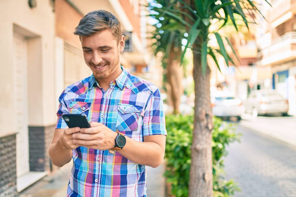 Young caucasian man smiling happy using smartphone at the city. - Fotoğraf, Görsel