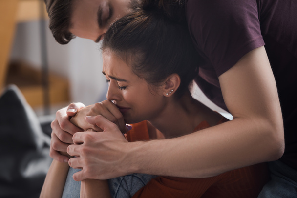 Молодой человек трогает руки и целует голову плачущей, подавленной женщины - Фото, изображение