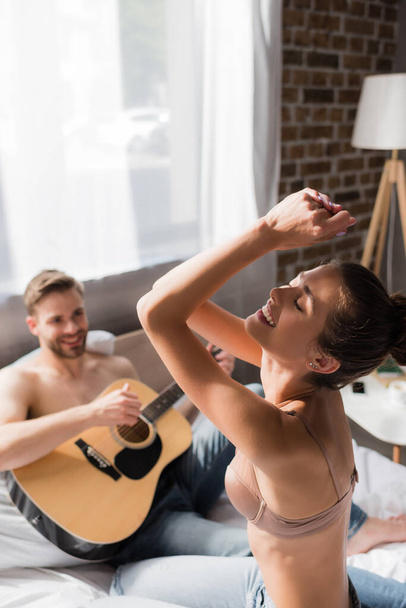 excited sexy woman dancing with closed eyes near man playing guitar on blurred background - 写真・画像