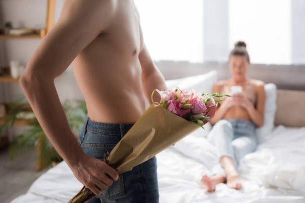 shirtless man holding bouquet while girlfriend chatting on smartphone on blurred background - Fotografie, Obrázek