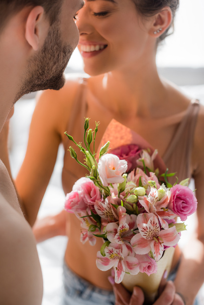 man holding flowers near smiling sexy girlfriend on blurred background - Fotografie, Obrázek