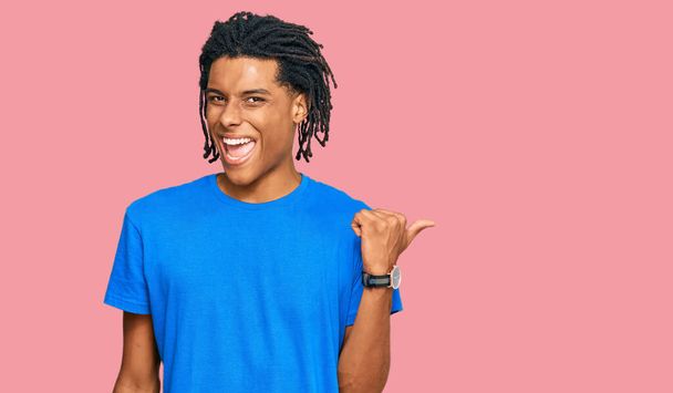 Jonge Afro-Amerikaanse man draagt casual kleding glimlachend met een vrolijk gezicht kijken en wijzen naar de zijkant met duim omhoog.  - Foto, afbeelding