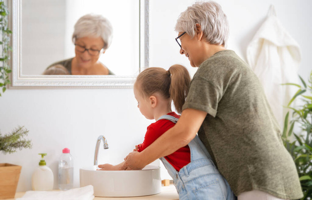 A cute little girl and her grandmother are washing their hands. Protection against infections and viruses.   - Фото, зображення