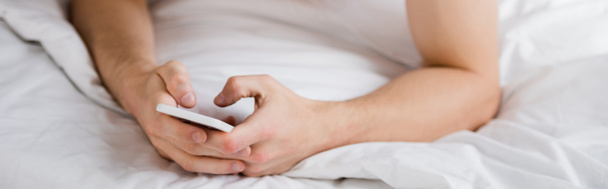 przycięty widok człowieka wiadomości na telefon komórkowy w łóżku, baner - Zdjęcie, obraz