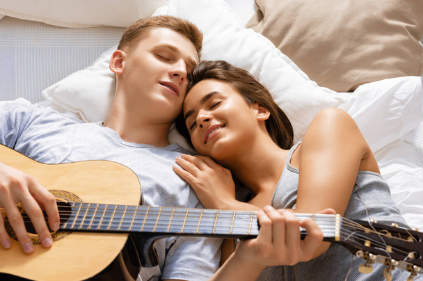 Happy couple in love. Stunning sensual portrait of young stylish fashion couple indoors. Young man playing guitar for his beloved girl. - Photo, Image