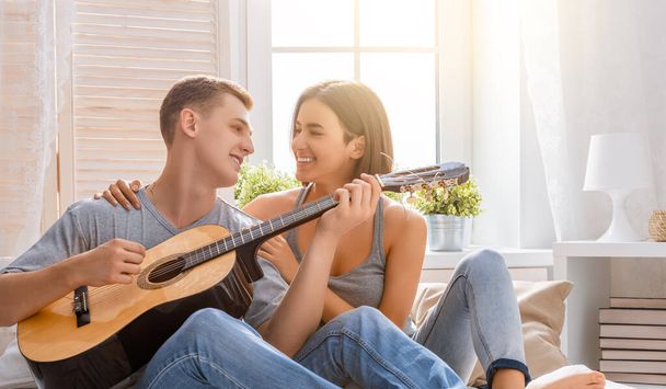 Happy couple in love. Stunning sensual portrait of young stylish fashion couple indoors. Young man playing guitar for his beloved girl. - Foto, immagini