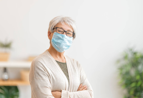 Senior woman wearing facemask during coronavirus and flu outbreak. Virus and illness protection, home quarantine. COVID-2019. Taking on or taking off masks. - Fotografie, Obrázek