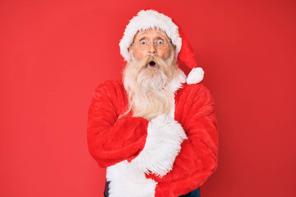 Oude senior man met grijs haar en lange baard draagt traditionele kerstman kostuum bang en geschokt met verrassende uitdrukking, angst en opgewonden gezicht.  - Foto, afbeelding