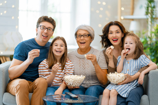 Happy family watching projector, TV, movies with popcorn  at home. Granny, mother, father and daughters spending time together. - Foto, Bild