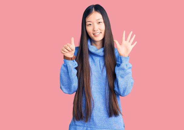 若いです美しいです中国の女性身に着けていますカジュアルturtleeckセーターショーと指差し指番号6ながら笑顔自信と幸せ.  - 写真・画像