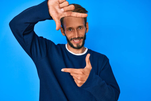 Handsome caucasian man with beard wearing casual sweater smiling making frame with hands and fingers with happy face. creativity and photography concept.  - Photo, image