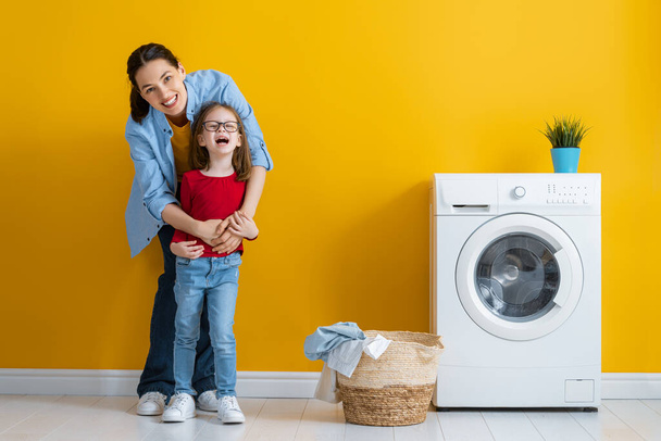 Beautiful young woman and child girl little helper are having fun and smiling while doing laundry at home. - Фото, зображення
