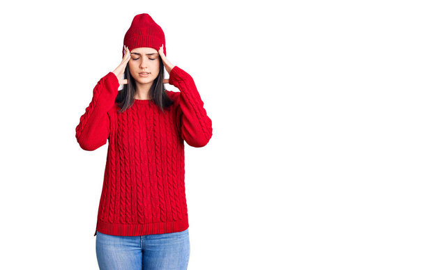 Молодая красивая девушка в свитере и шерстяной шапке с рукой на голове от боли в голове, потому что стресс. страдает мигренью.  - Фото, изображение