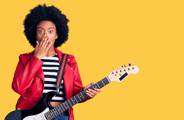 Young african american woman playing electric guitar covering mouth with hand, shocked and afraid for mistake. surprised expression  - Фото, изображение