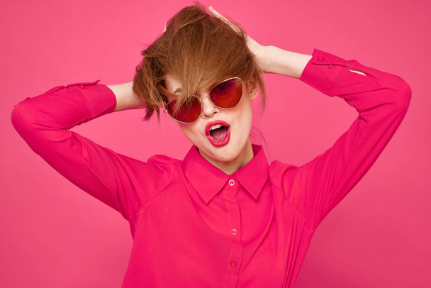 Весела жінка в сонцезахисних окулярах торкається волосся руками і рожевою сорочкою обрізаний вид
 - Фото, зображення