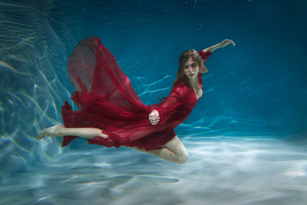 Beautiful slender girl in a long red dress underwater. - 写真・画像
