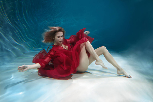 Beautiful slender girl in a long red dress underwater. - Photo, image