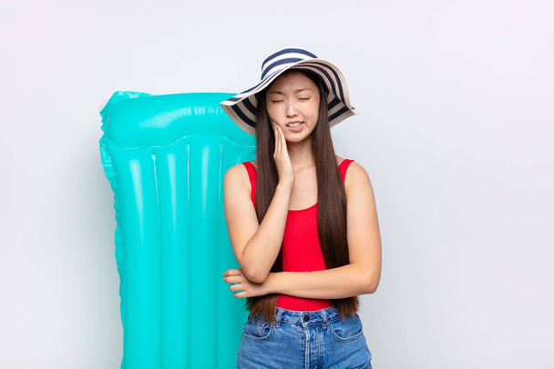 asian young woman holding cheek and suffering painful toothache, feeling ill, miserable and unhappy, looking for a dentist. summer concept - 写真・画像