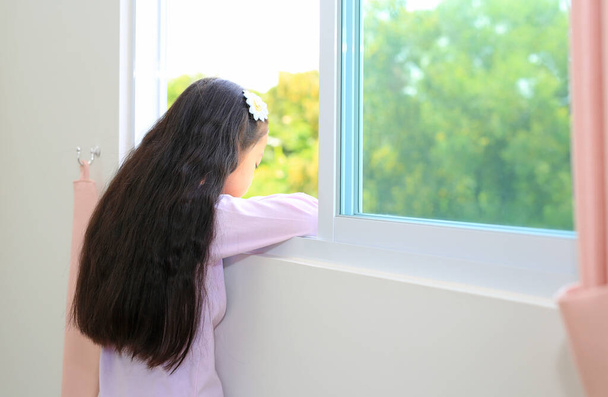 Caucasian little kid girl lies at window of house and watching out. Back view. - Foto, imagen