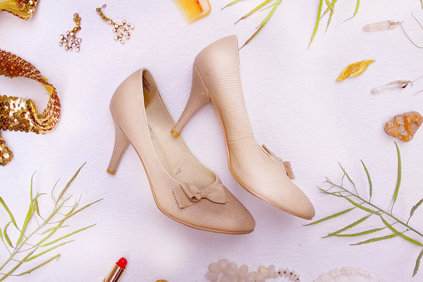 Flat lay retro beige shoes, golden earings, accesories, trendy grass, lip stick, upper view. - Фото, изображение