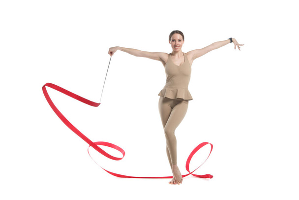 štíhlá půvabná dívka gymnastka v béžové sportovní oblečení tanec s červenou rozvíjející stuhou izolované na bílém pozadí. - Fotografie, Obrázek