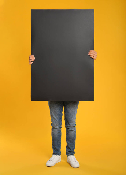 Man holding black blank poster on yellow background. Mockup for design - Foto, imagen
