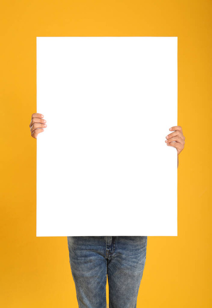 Man holding white blank poster on yellow background. Mockup for design - Foto, afbeelding