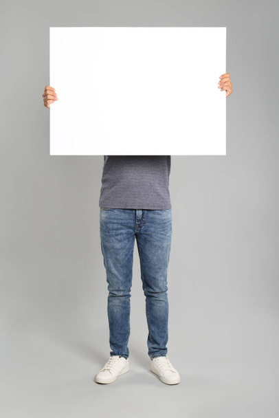 Man holding white blank poster on grey background. Mockup for design - Фото, зображення