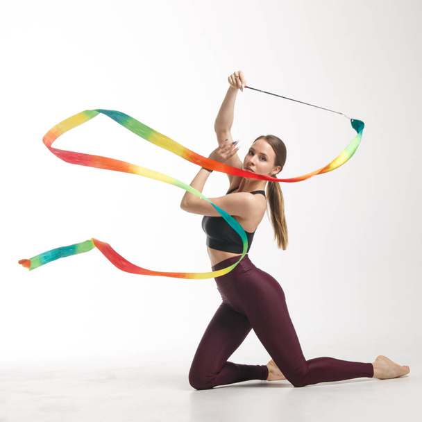 Young slim girl gymnast in sportswear is training with a multi-colored ribbon isolated on white background. - Φωτογραφία, εικόνα
