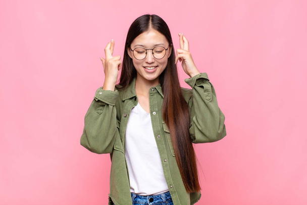 asian young woman smiling and anxiously crossing both fingers, feeling worried and wishing or hoping for good luck - Фото, изображение