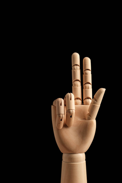 A mão de madeira do manequim do desenho mostra três dedos em um fundo preto. Aprender a contar - três. Vista lateral. Modelo de arte para desenho. Parte do corpo - mão, escova. - Foto, Imagem