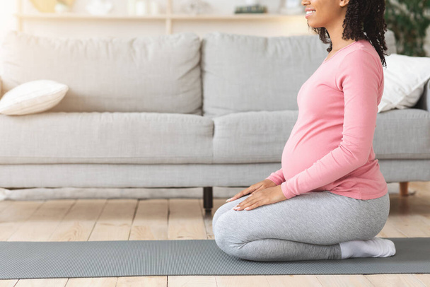 Schwangere schwarze Frau sitzt auf Matte und bereitet sich vor dem Training vor - Foto, Bild