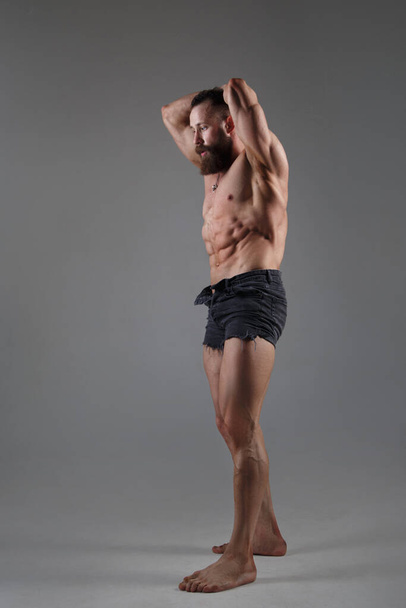 Athletic muscular man in some shorts is standing in full growth isolated on a gray background. - 写真・画像