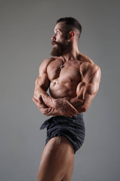 Athletic muscular man in some shorts demonstrates muscles isolated on a gray background. - Foto, Bild