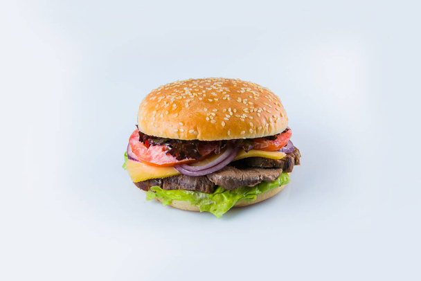 Marha burger zöldségekkel és sajttal búzakenyérben szezámmaggal. Hús borjú Burger friss saláta levelek, paradicsom, spanyol hagyma izolált fehér alapon. Élelmiszer elkülönítés  - Fotó, kép