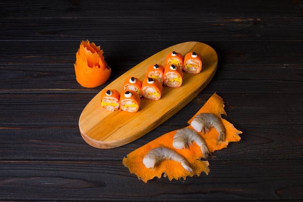 Primo piano di tempura giapponese gamberetti rotolo di sushi senza riso avvolto in daikon carota servito su piatto di legno. Tre gamberetti tigre neri crudi su fette di carota vicino a frutti di mare sani nessun piatto di riso - Foto, immagini