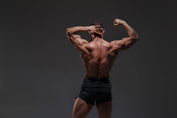 Portrait of a  athletic man with a naked torso showing muscles isolated on a dark gray background, view from the back. - Foto, immagini