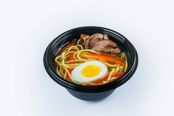 Σούπα βοδινού Udon με αυγό, ζυμαρικά udon και φιλέτο βοδινού, πάπρικα (bell pepper) σερβίρεται σε πλαστικό μπολ παράδοσης. Πιάτα απομονώνονται σε γκρι φόντο. Ασιατικό πρώτο πιάτο σε μαύρο πιάτο. Απομόνωση τροφίμων - Φωτογραφία, εικόνα