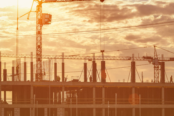 Silhouette eines Bauarbeiterteams und eines Krans beim Bau eines Gebäudes vor dem Hintergrund des abendlichen Sonnenuntergangs. - Foto, Bild