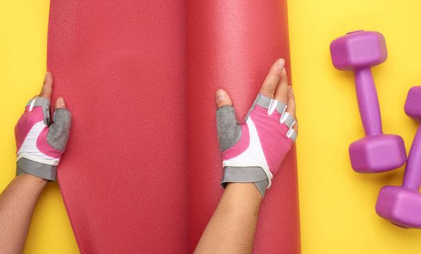 Női kéz a sport kesztyű kibontakozik egy piros sport szőnyeg sárga alapon, felső nézet. - Fotó, kép