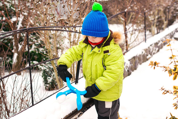 Glückliches Kind, das Spaß beim Winterspaziergang hat. Kleiner Junge spielt mit Schneeballmacher. Schneekaltes Wetter. Beliebtes Spielzeug für Kinder zur Herstellung von Schneebällen. Kind bastelt Schneebälle. - Foto, Bild